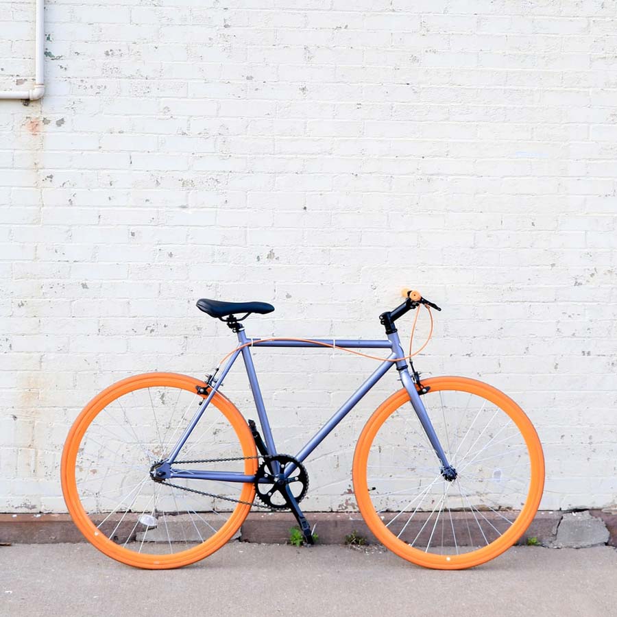 Bike with orange wheels leaning against white brick wall