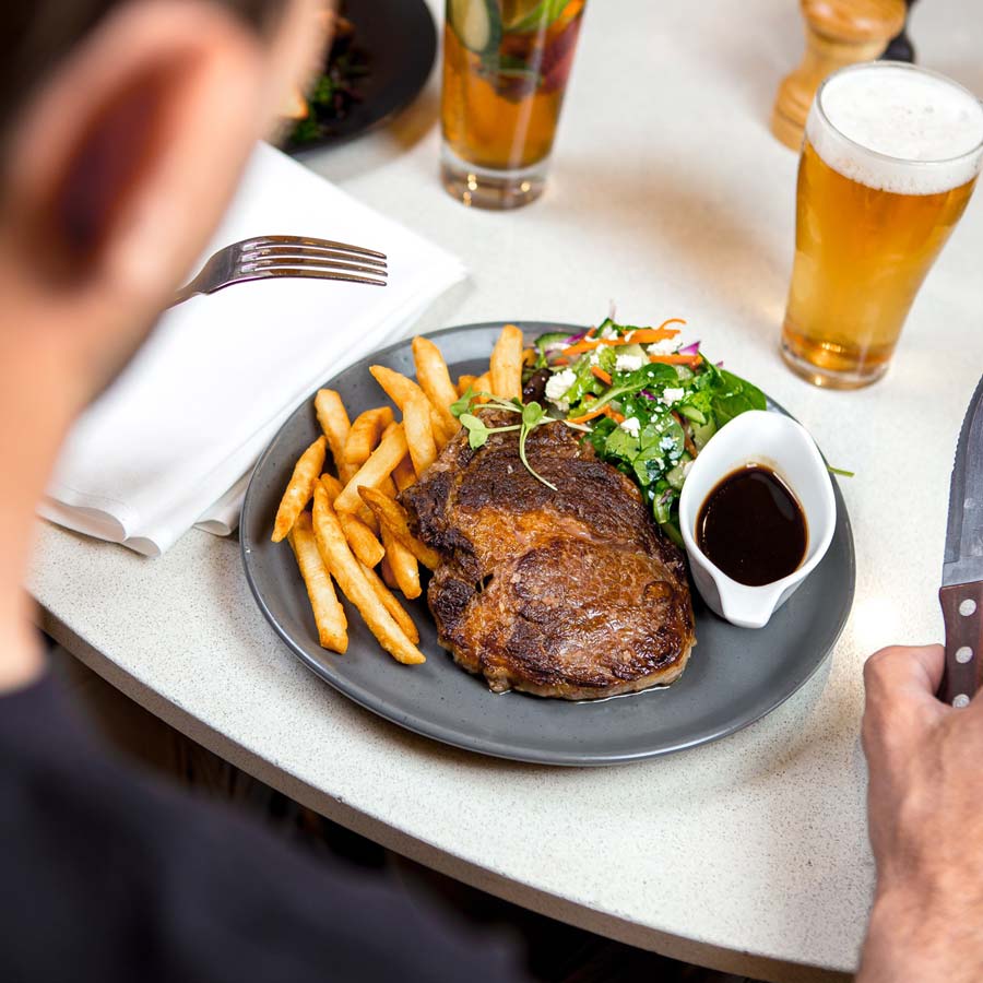 Man looking down at his steak, chips and salad with a beer