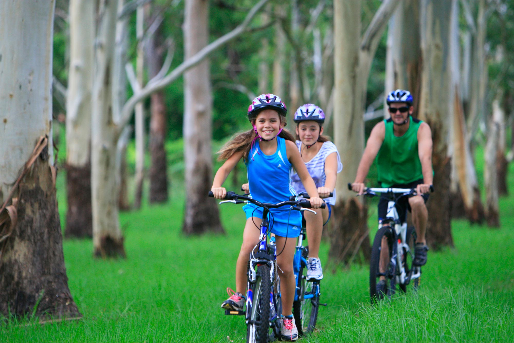 Smiling family riding bikes through green grass